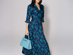 Woman wearing a blue floral dress holding a large turquoise , ‘croc’ print Italian calf leather handbag with top handle, detachable strap and gold plated hardware against a plain background