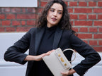 Woman holding a beige Italian leather handbag with gold hardware on a white background