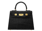 Black ‘crocodile print’ handbag with gold hardware on a white background