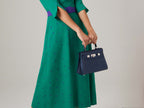 Person wearing a green dress with purple polka dots holding a Medium navy blue natural grain Italian leather handbag with a hint of silver sparkle with silver hardware, a top handle and a detachable strap against a neutral background