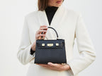 Woman holding a black calf Italian leather handbag with a pebble print texture, featuring a top handle, detachable strap and gold-plated hardware.