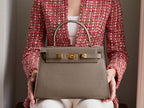 Woman holding a large taupe coloured, natural grainy print Italian calf leather handbag with top handle, detachable strap and gold plated hardware.