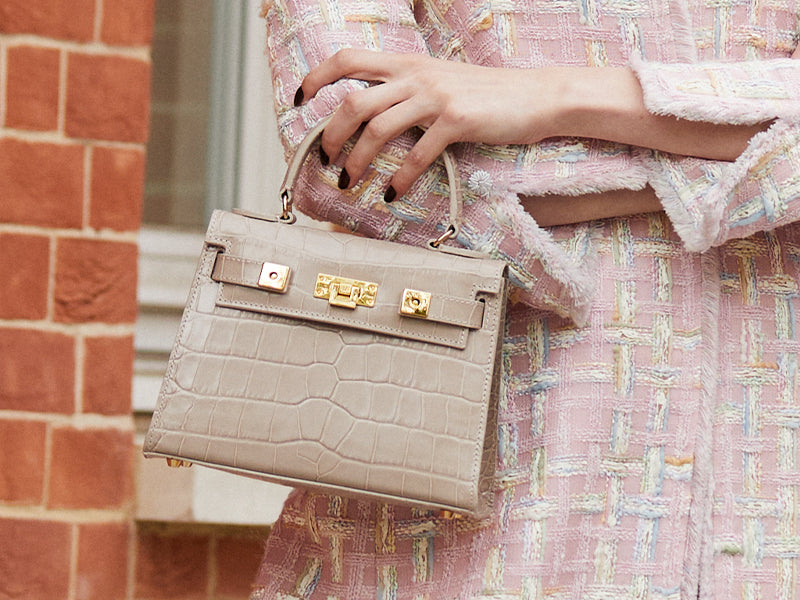 Woman carrying a stone croc print Italian calf leather luxury handbag with gold plated hardware and a top handle.