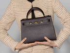 Person holding a large brown Italian leather, natural print handbag with gold hardware, a top handle with a detachable strap on a white background against a neutral background