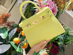 A bright yellow luxury Italian leather natural soft grain handbag with a top handle, detachable strap and gold-plated hardware, positioned against a plain background.