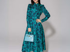 Woman wearing a green patterned dress holding a turquoise 'Croc' print Italian calf leather handbag with gold plated hardware and a top handle against a gray background