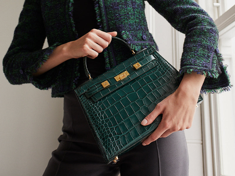 Woman holding a large dark green ‘croc’ print Italian calf leather handbag with top handle, detachable strap and gold plated hardware