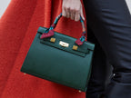 Woman carrying a large dark green pebble print Italian calf leather handbag with top handle, detachable strap and gold plated hardware