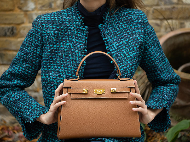 Woman holding a large tan pebble print Italian calf leather handbag with top handle, detachable strap and gold plated hardware