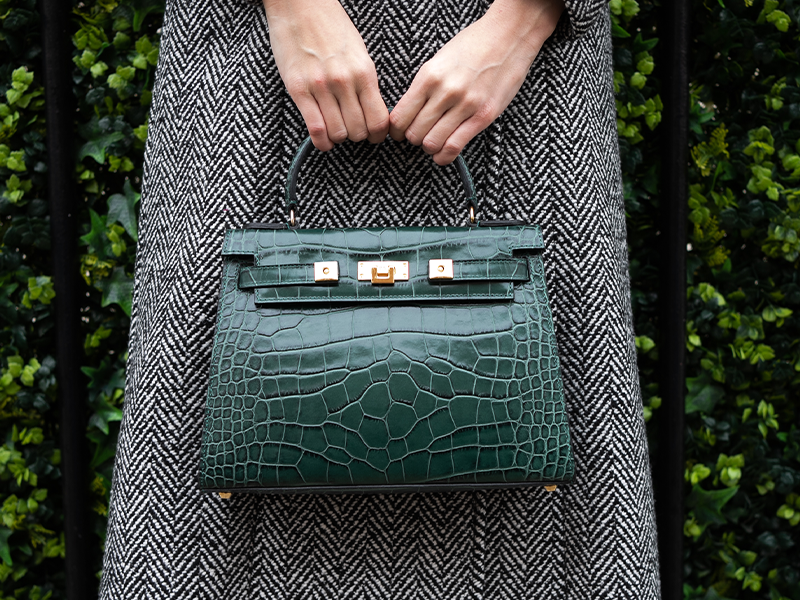 Woman carrying a large dark green ‘croc’ print Italian calf leather handbag with top handle, detachable strap and gold plated hardware